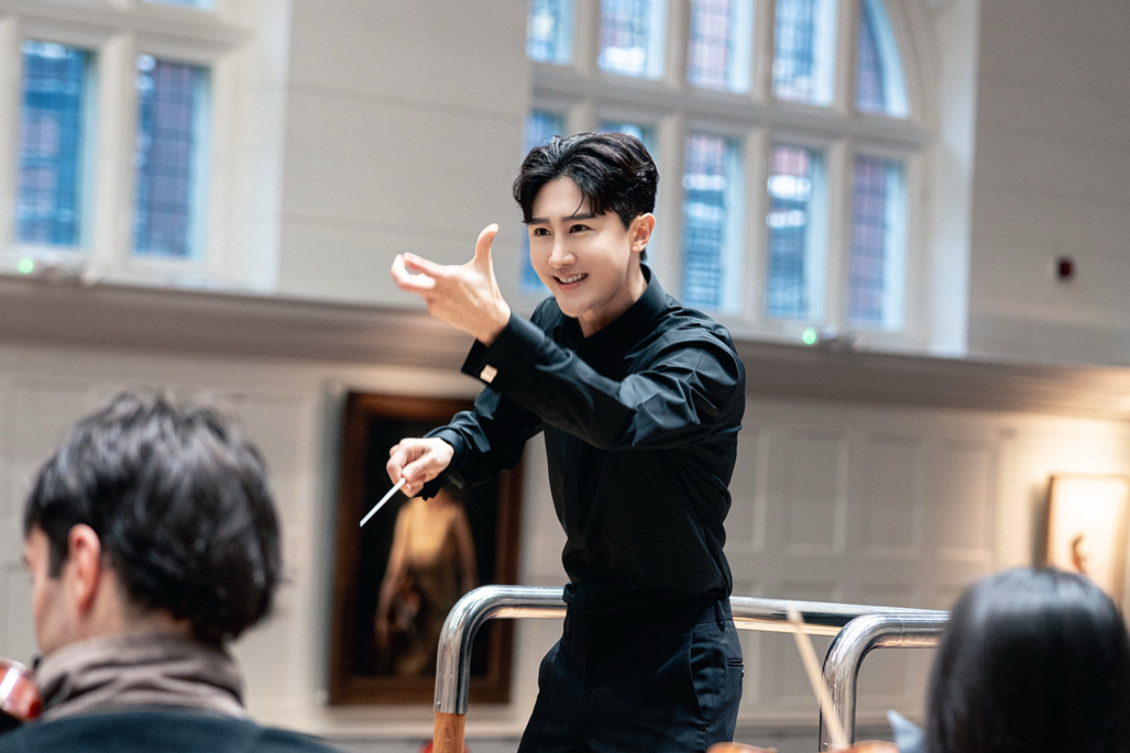 An Asian male student conducting an orchestra rehearsal.